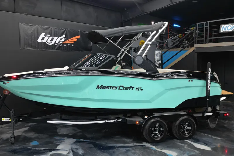 The Image of 2024 MasterCraft NXT21 boat in showroom, turquoise hull, black accents, on trailer. - 1