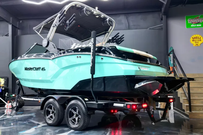 Slide: The Image of 2024 MasterCraft NXT21 boat in showroom, vibrant teal and black design on trailer. - 3
