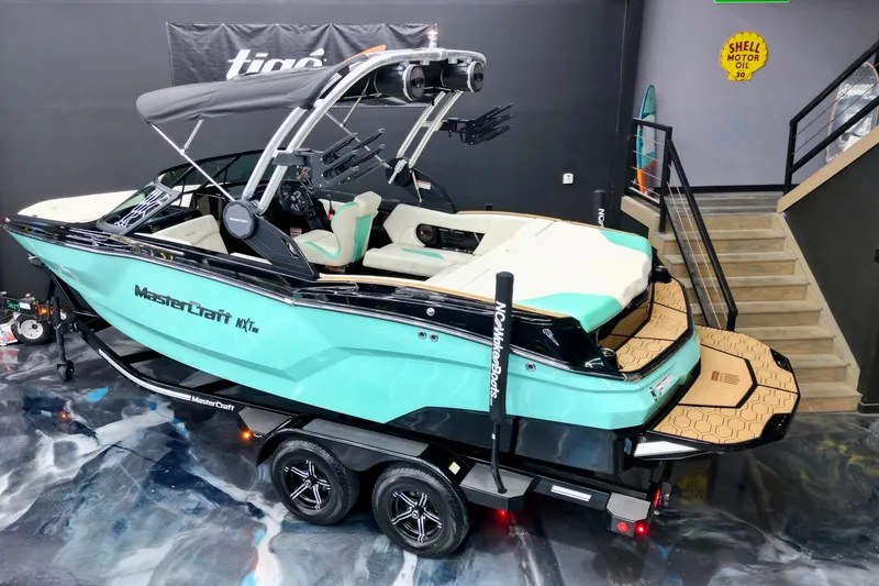 Slide: The Image of 2024 MasterCraft NXT21 boat in showroom, teal and black design, on trailer. - 4