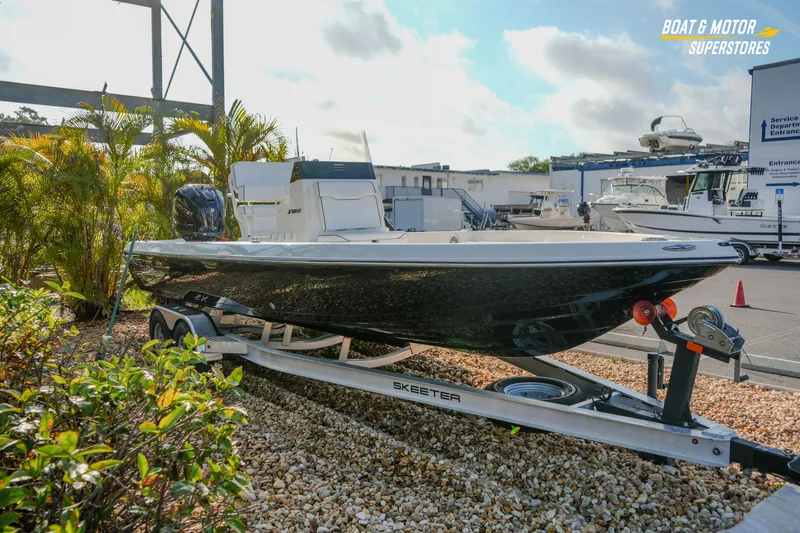 Slide: The Image of 2026 Skeeter SX230 boat on trailer at dealership, surrounded by plants and other boats. - 9
