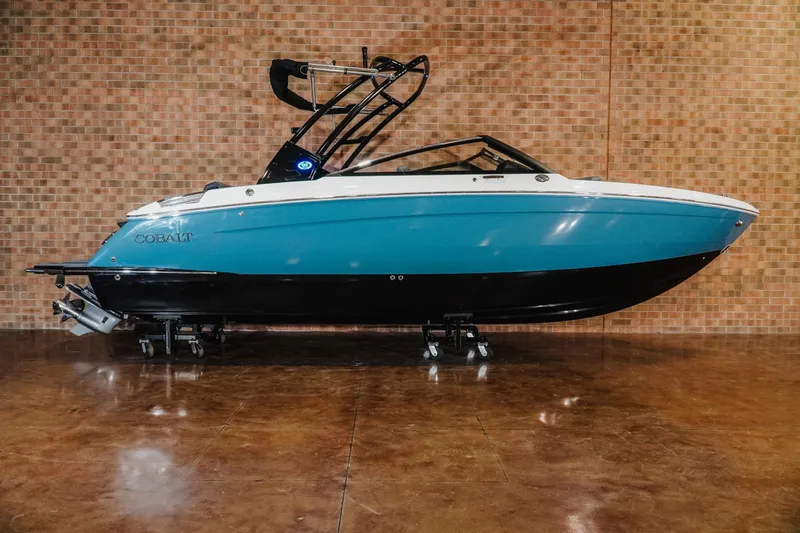 The Image of 2026 Cobalt R6 boat with blue and black hull, displayed indoors against brick wall. - 1