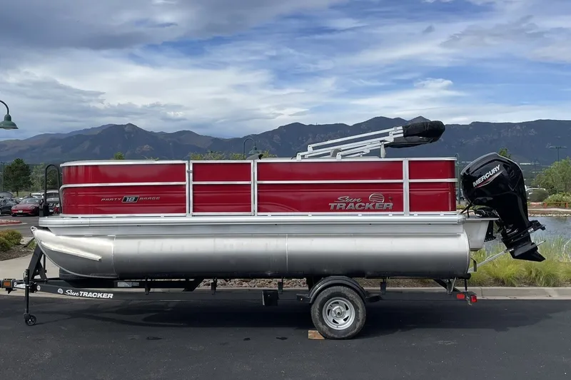 The Image of 2026 Sun Tracker Party Barge 18 DLX pontoon boat with Mercury engine, parked with mountain backdrop. - 0
