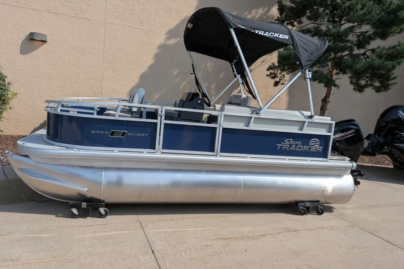 The Image of 2026 Sun Tracker Bass Buggy 16 XL Select pontoon boat with canopy, parked outdoors. - 0