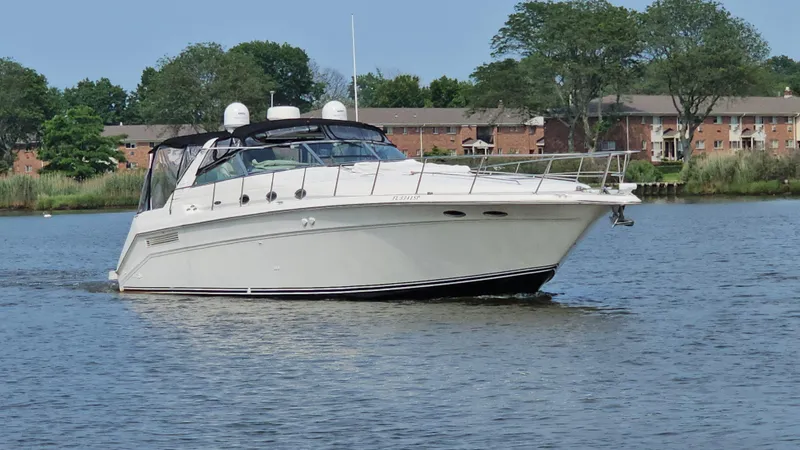 Slide: The Image of 1999 Sea Ray 500 Sundancer yacht cruising on a calm river near residential buildings. - 2