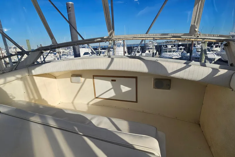 Slide: The Image of 1980 Bertram 42 Convertible boat interior with marina view, featuring white seating and clear canopy. - 33