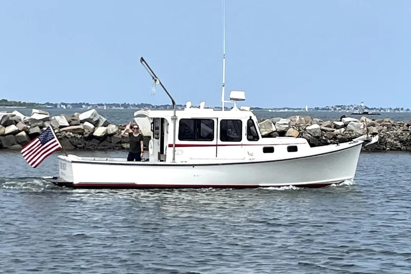 Slide: The Image of 1988 Duffy 31 Lobster Boat cruising near rocky shoreline with American flag. - 11