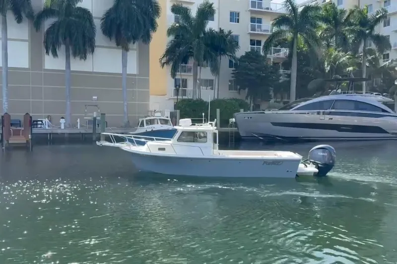 Slide: The Image of 2023 Parker 2320 Sport Cabin boat cruising near palm trees and buildings. - 2