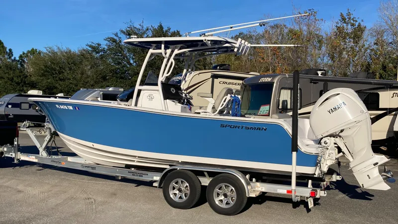The Image of 2023 Sportsman Open 242 Center Console boat on trailer, blue hull, parked outdoors. - 0