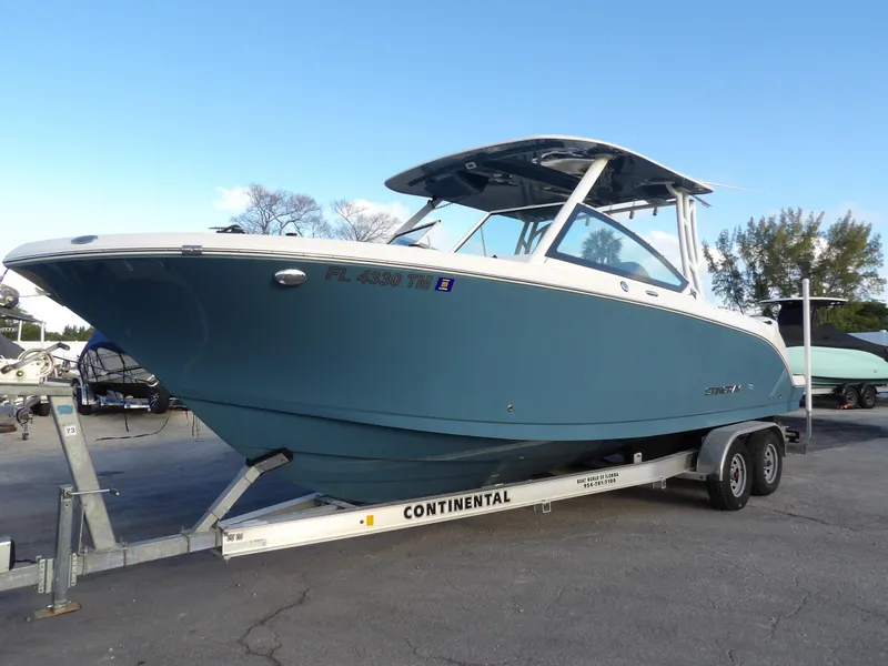 The Image of 2022 Stingray 269 DC boat on trailer, blue hull, parked outdoors. - 0