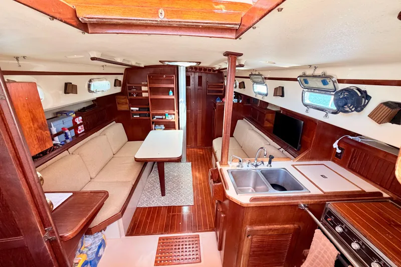 Slide: The Image of 1989 Island Packet Cutter interior with wood finish, cozy seating, and compact kitchen area. - 3