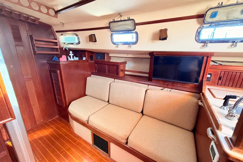 Slide: The Image of 1989 Island Packet Cutter interior with wooden finish, beige sofa, and porthole windows. - 7