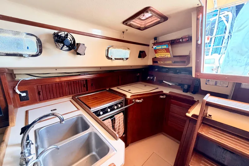 Slide: The Image of 1989 Island Packet Cutter yacht kitchen with dual sink, stove, and wooden cabinetry. - 8