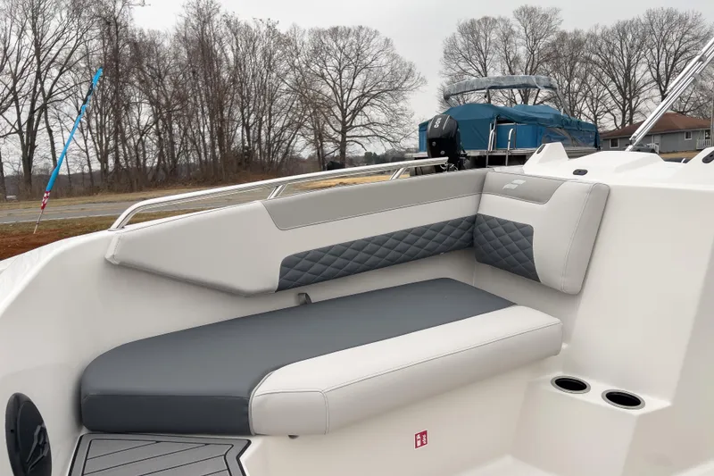 Slide: The Image of 2026 Starcraft SVX 171 OB boat interior with gray and white seating, cup holders, and trees in background. - 7