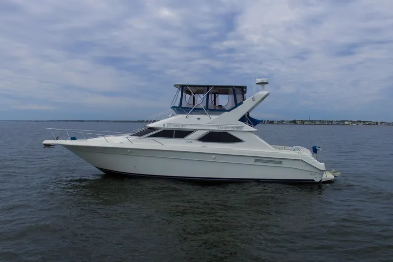 Slide: The Image of 1993 Sea Ray 440 Express Bridge yacht on calm waters under a cloudy sky. - 1