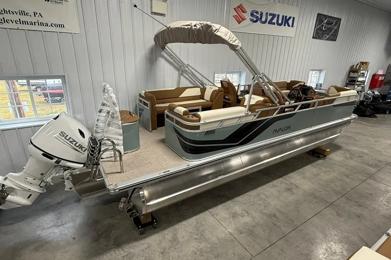 The Image of 2026 Avalon Venture Quad Lounge 19' pontoon boat in showroom with Suzuki outboard motor. - 1