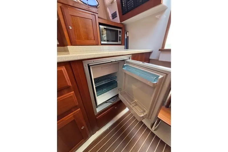 Slide: The Image of 2018 Back Cove 30 yacht kitchen with open fridge, microwave, and wooden cabinetry. - 30