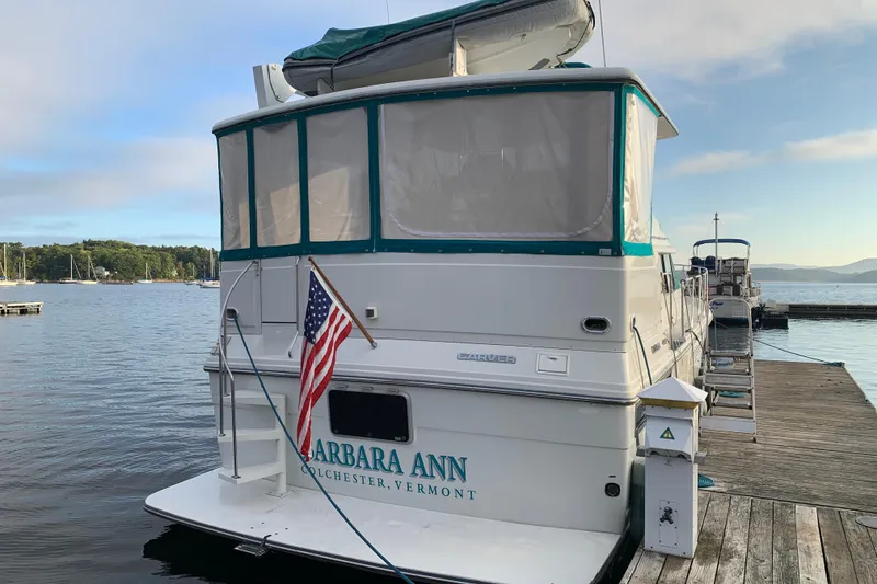 Slide: The Image of 1994 Carver 440 Aft Cabin Motor Yacht docked, displaying American flag, serene waterfront setting. - 5