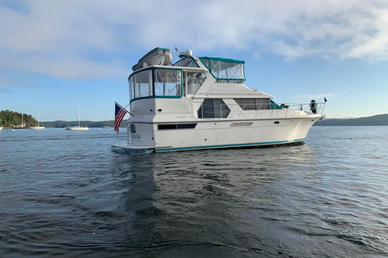 Slide: The Image of 1994 Carver 440 Aft Cabin Motor Yacht on serene water with clear sky backdrop. - 54