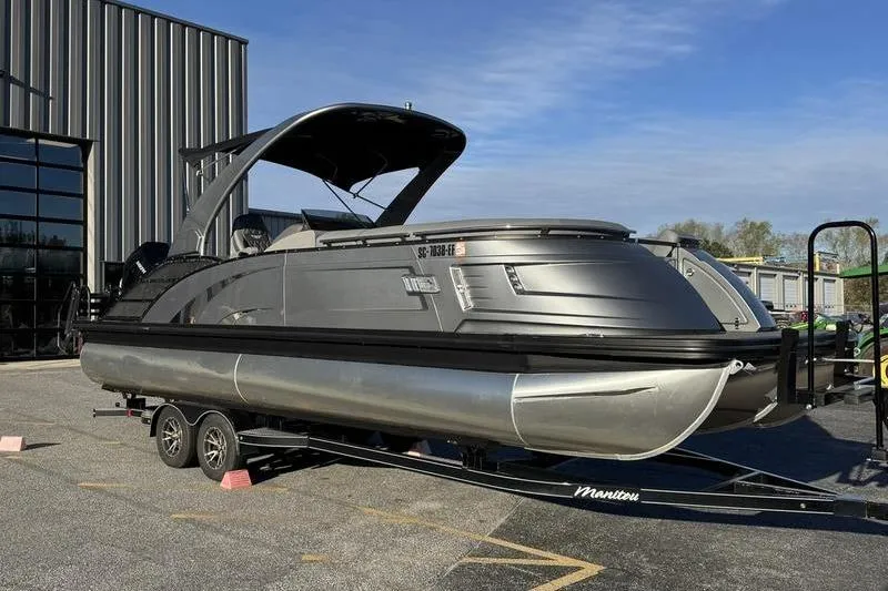 Slide: The Image of 2024 Bennington 25 QXSBA pontoon boat on trailer, parked outdoors. - 5