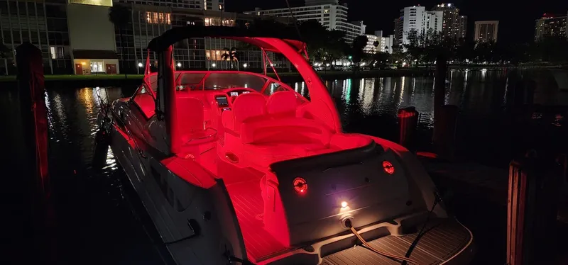 Slide: The Image of 2004 Sea Ray 340 Sundancer boat with red interior lighting at night, docked in a city marina. - 23