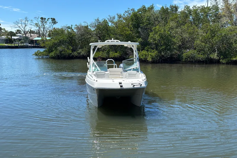 Slide: The Image of 2025 World Cat 230 SD boat navigating calm waters near lush greenery. - 2