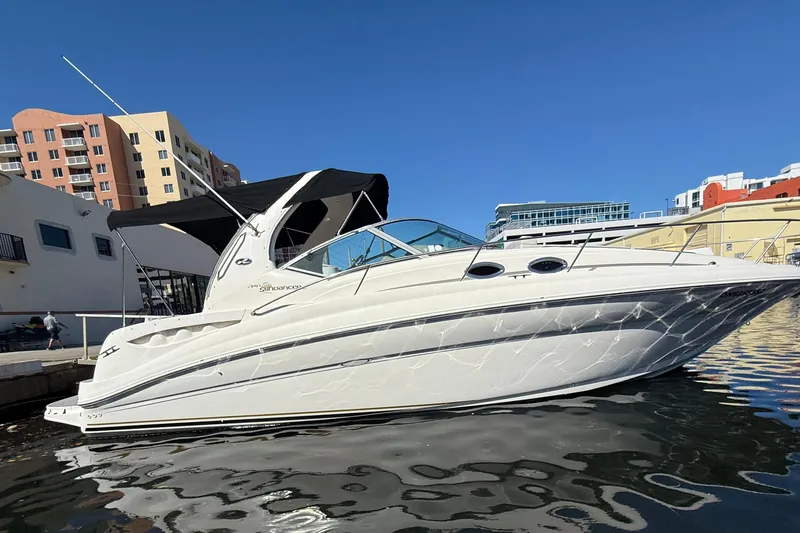 The Image of 2003 Sea Ray 320 Sundancer yacht docked in urban marina under clear blue sky. - 0