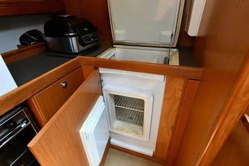 Slide: The Image of 2016 Bavaria Cruiser 41 yacht kitchen with open fridge and wooden cabinetry. - 26
