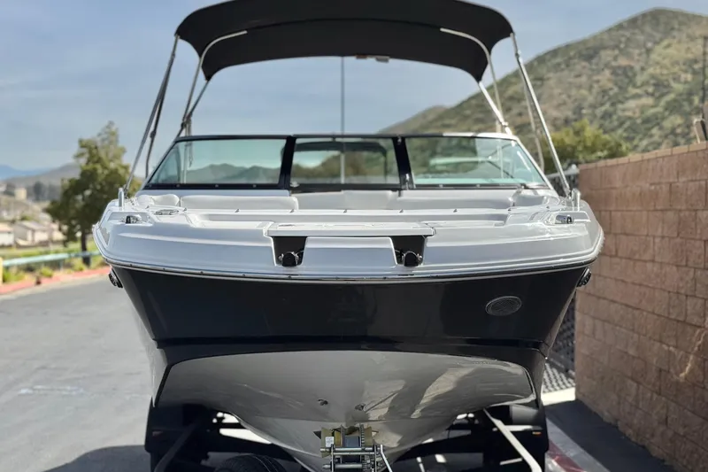 Slide: The Image of 2023 Four Winns HD3 boat with canopy, parked outdoors, mountainous background. - 2