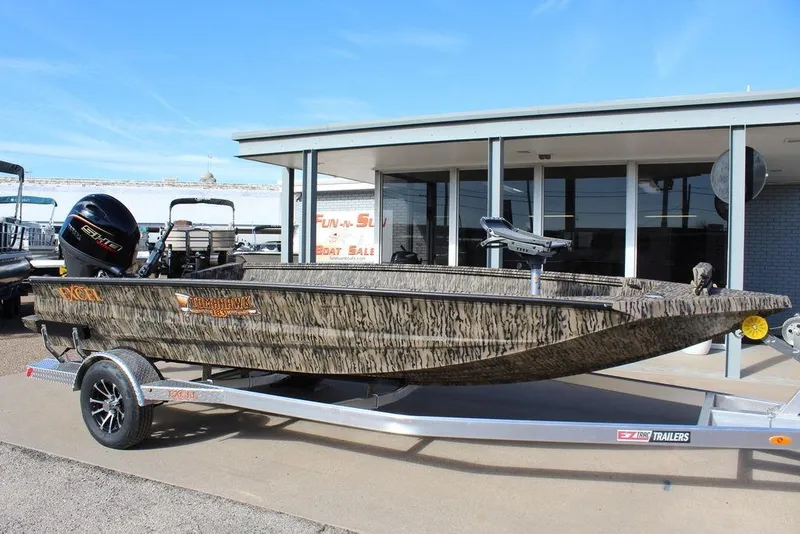 The Image of 2026 Excel 183 Tomahawk boat on trailer, camo design, outside dealership. - 1