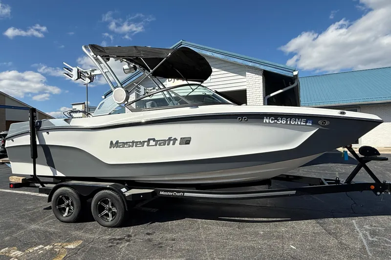 Slide: The Image of 2023 MasterCraft XT22 boat on trailer, parked outdoors under blue sky. - 2