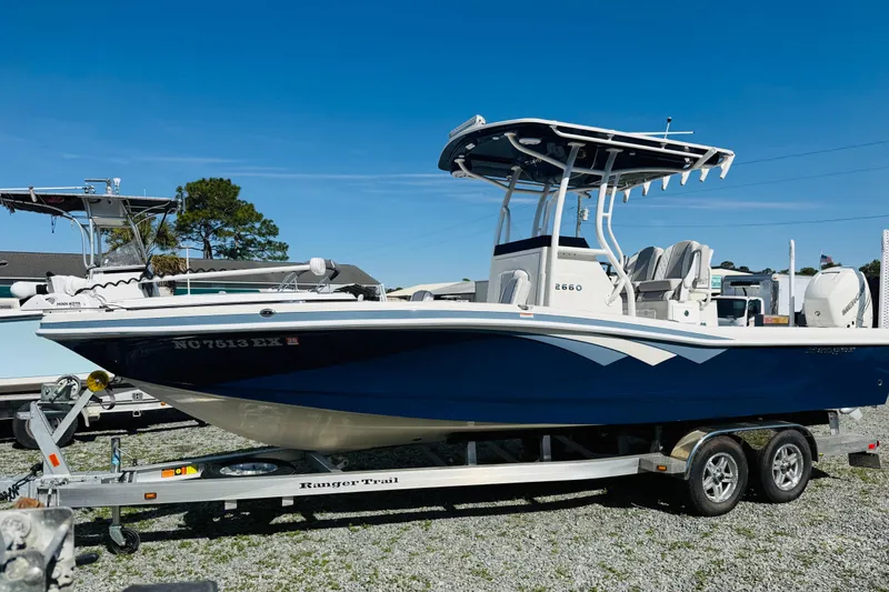 Slide: The Image of 2022 Ranger 2660 Bay boat on trailer, blue hull, clear sky background. - 2