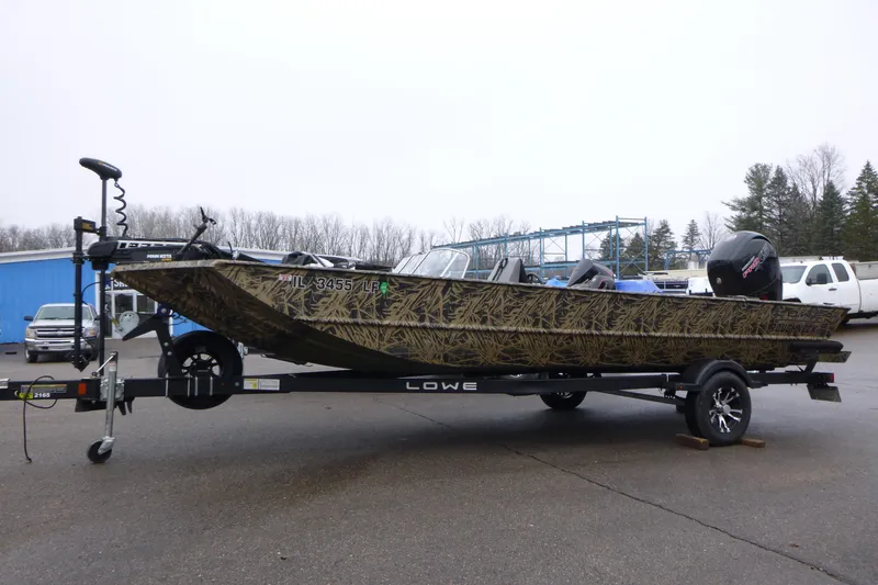 The Image of 2024 Lowe Roughneck 2070 boat on trailer, camo design, parked outdoors. - 1