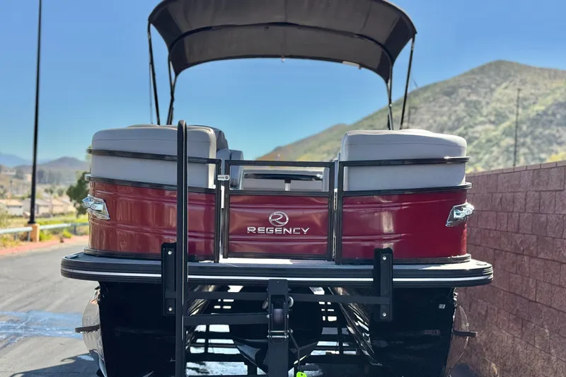Slide: The Image of 2023 Regency 250 DL3 pontoon boat with red exterior, parked near scenic mountains. - 2