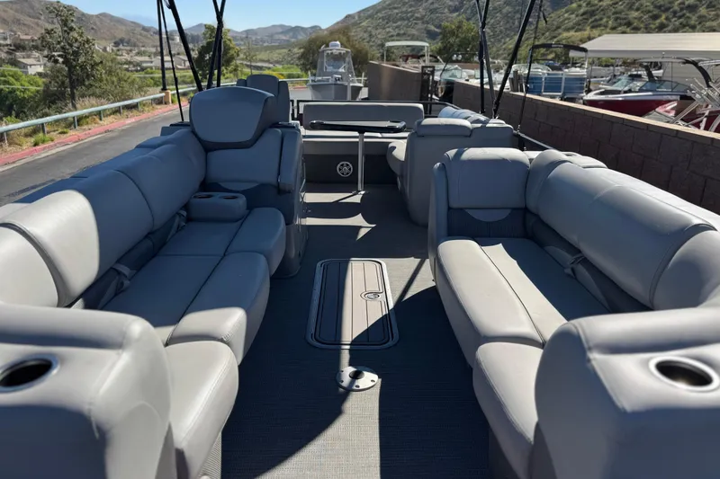 Slide: The Image of 2023 Regency 250 DL3 pontoon boat interior with plush seating and scenic mountain backdrop. - 9