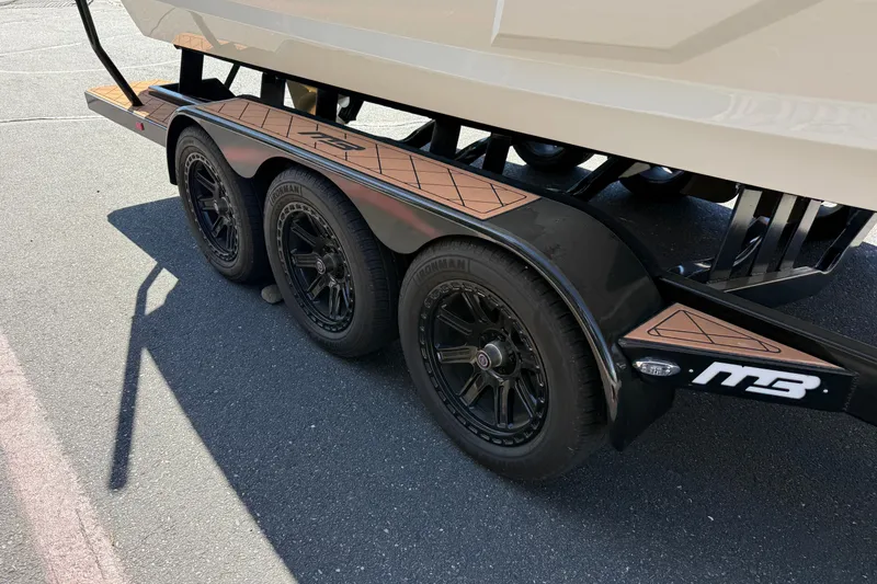 Slide: The Image of 2025 MB B52 25 Alpha boat trailer with black wheels on pavement. - 10