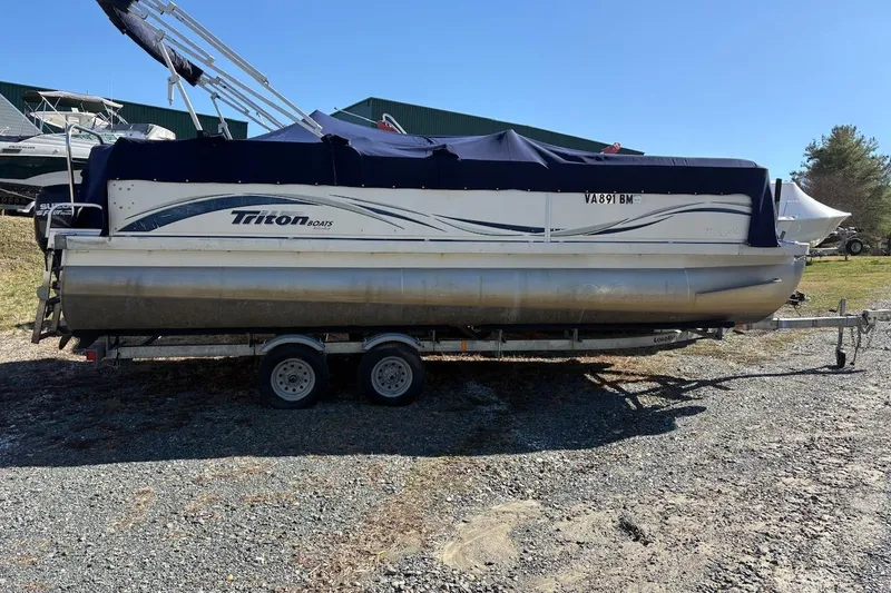 The Image of 2006 Triton 220 F Gold pontoon boat on trailer, covered and parked outdoors. - 0