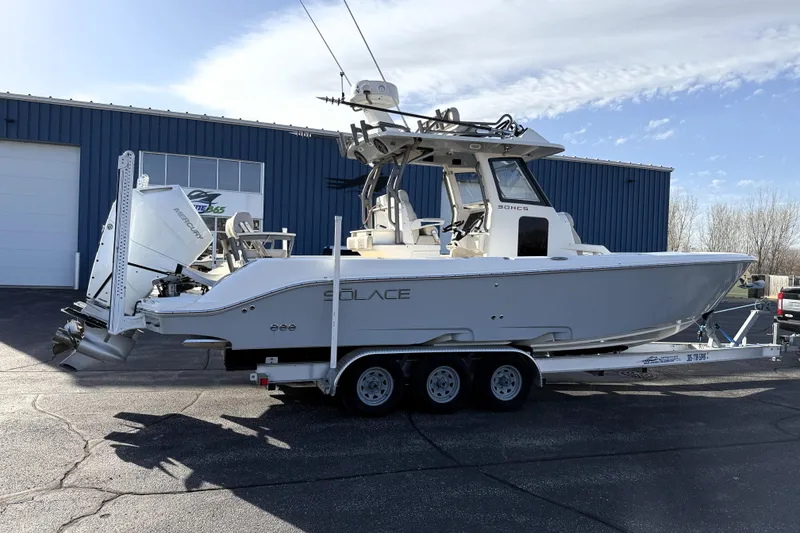 Slide: The Image of 2023 Solace 30 HCS boat on trailer, parked outside a blue industrial building. - 2