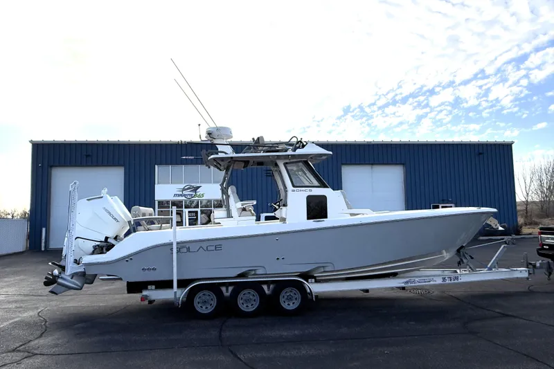 Slide: The Image of 2023 Solace 30 HCS boat on trailer, parked outside a blue industrial building. - 7