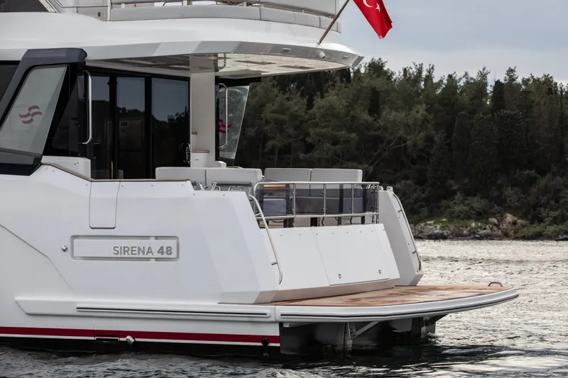 Slide: The Image of 2027 Sirena 48 yacht with Turkish flag, docked near lush green shoreline. - 14