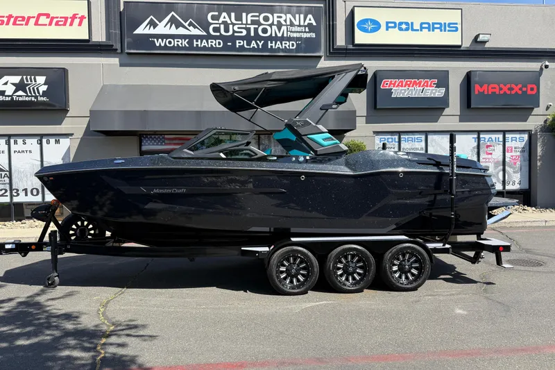 Slide: The Image of 2026 MasterCraft X24 boat on trailer outside dealership, featuring sleek black design. - 1