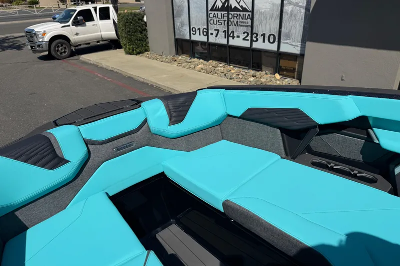Slide: The Image of 2026 MasterCraft X24 boat interior with turquoise and black seating, parked outside a building. - 55