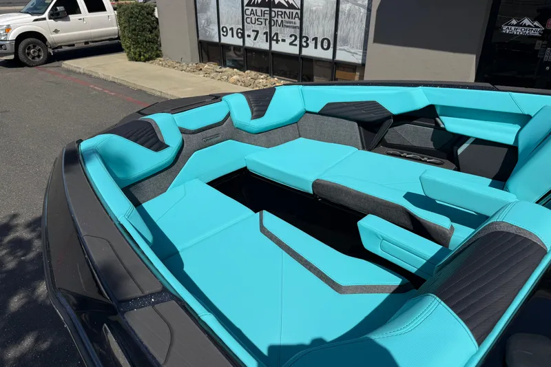 Slide: The Image of 2026 MasterCraft X24 boat interior with turquoise and black seating, parked outside a building. - 73