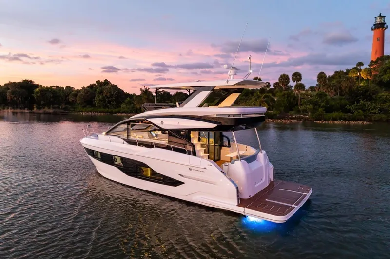 Slide: The Image of 2026 Cruisers Yachts 50 Fly at sunset on tranquil water, near lush greenery. - 9