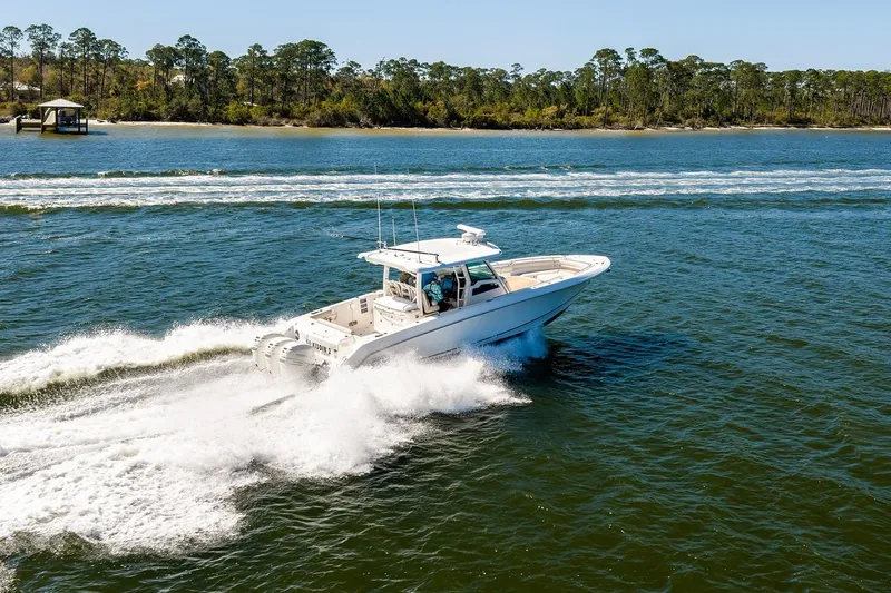 Slide: The Image of 2018 Boston Whaler 380 Outrage cruising on open water near a forested shoreline. - 15