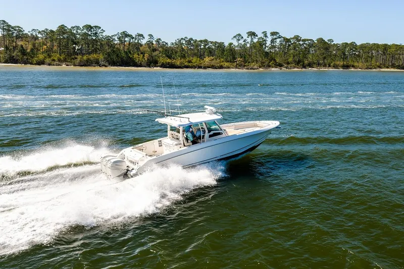 Slide: The Image of 2018 Boston Whaler 380 Outrage cruising on open water near a forested shoreline. - 16