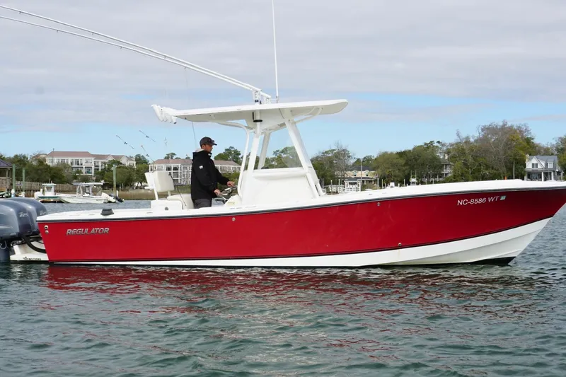 Slide: The Image of 2003 Regulator 26 Forward Seating boat with red hull on calm water. - 2