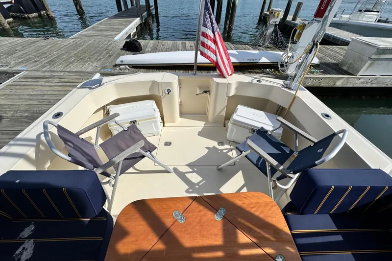 Slide: The Image of 2004 Mainship Pilot 30 Rum Runner boat interior with seating, table, and American flag at dock. - 21