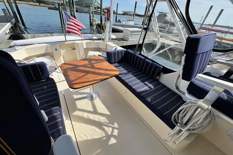 Slide: The Image of 2004 Mainship Pilot 30 Rum Runner boat interior with seating and table, docked by the water. - 28