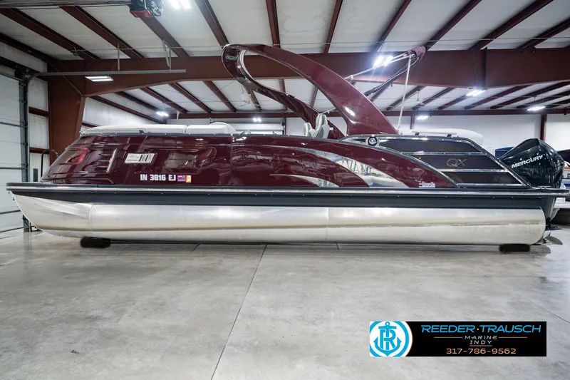 Slide: The Image of 2022 Bennington 23 QXFBA pontoon boat in a showroom, featuring sleek maroon design. - 10
