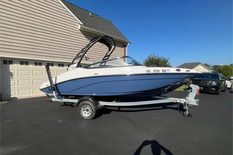 The Image of 2024 Yamaha Boats 195S on trailer, parked in driveway under clear blue sky. - 0